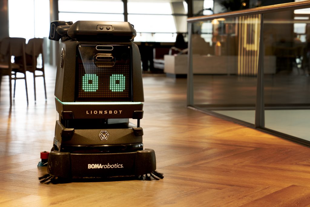 Autonomous cleaning robot operating in a modern office environment with wooden floors.